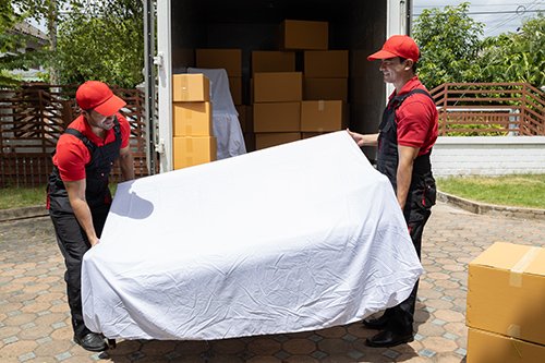 Portrait of two movers unloading boxes and furniture from a pickup truck.